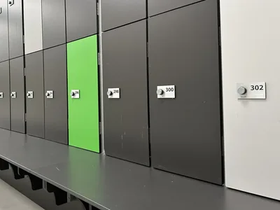 Hilera de taquillas fenólicas de un gimnasio con cerradura RFID Ojmar y placa numerada en cada puerta, sobre su banco