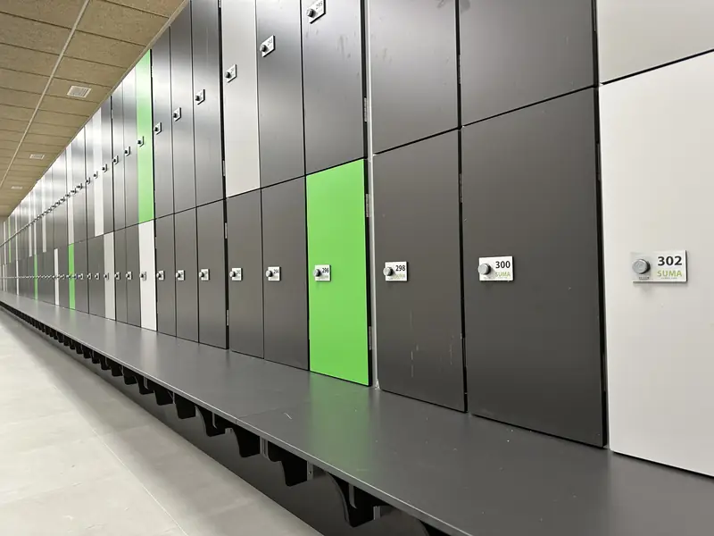 Fila de taquillas fenólicas grises y verdes con banco en un vestuario