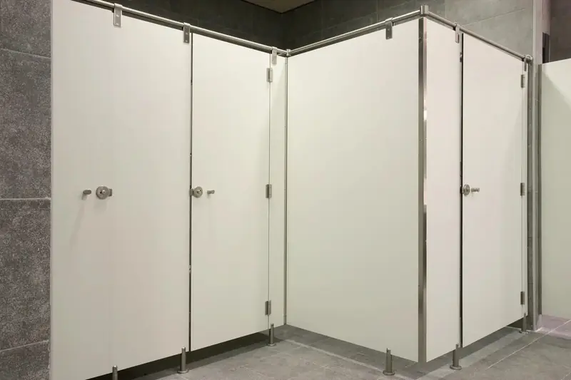 Cabinas sanitarias blancas en L, con las esquinas de acero inoxidable