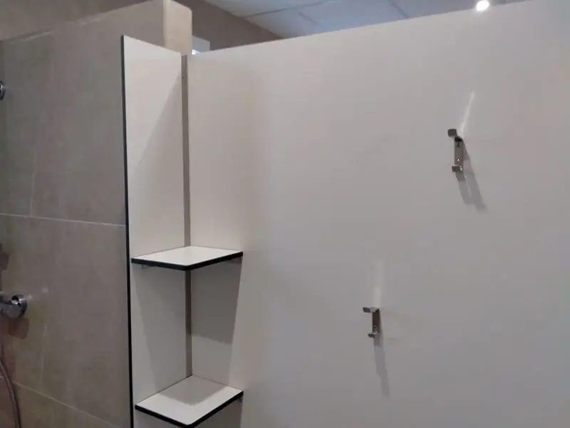 Ducha de compacto fenólico blanco con repisas del mismo material y ganchos para la toalla