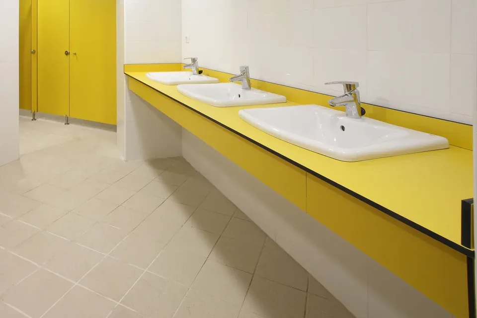 Encimera fenólica amarilla con el copete de serie, bajo, contra la pared y el faldón delante, con tres lavabos encastrados