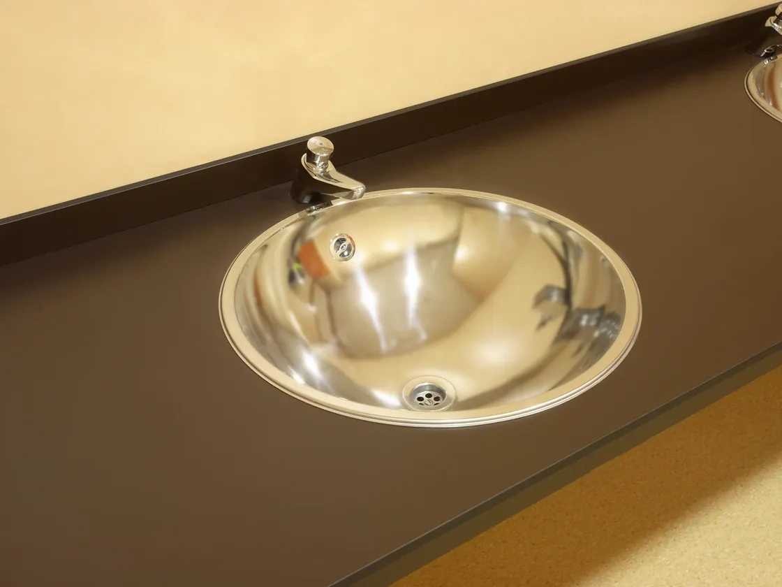 Lavabo de acero inoxidable encastrado en una encimera fenólica oscura, con el borde apoyado sobre el tablero