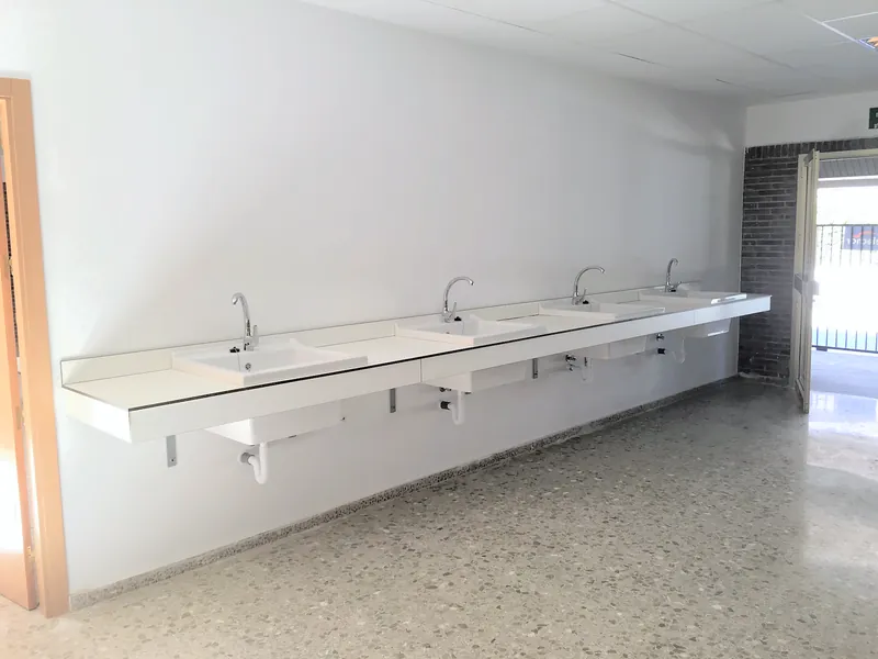 Encimera fenólica blanca larga con lavabos encastrados, sobre escuadras metálicas a la pared