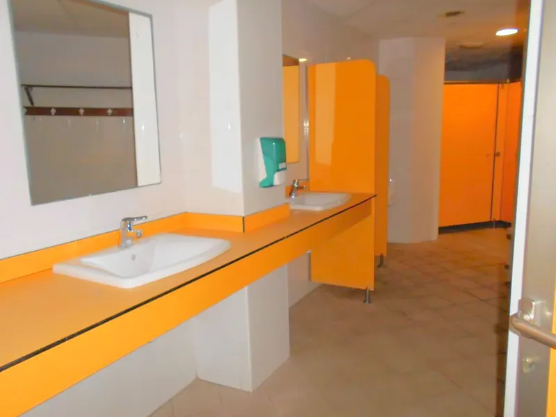 Encimera fenólica naranja con lavabos encastrados en un aseo con cabinas naranjas