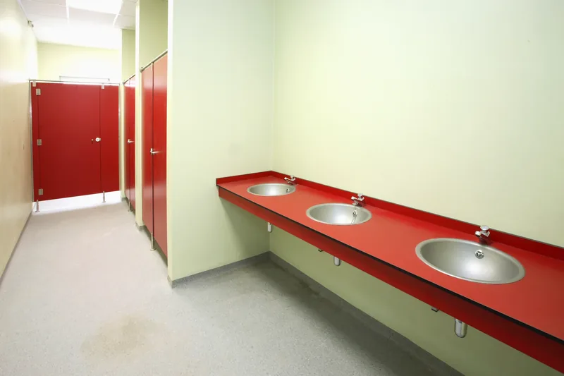 Encimera fenólica roja con lavabos de acero inoxidable encastrados en el pasillo de un aseo