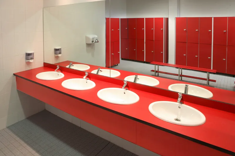 Encimera fenólica roja con cuatro lavabos encastrados en un vestuario con taquillas rojas a juego