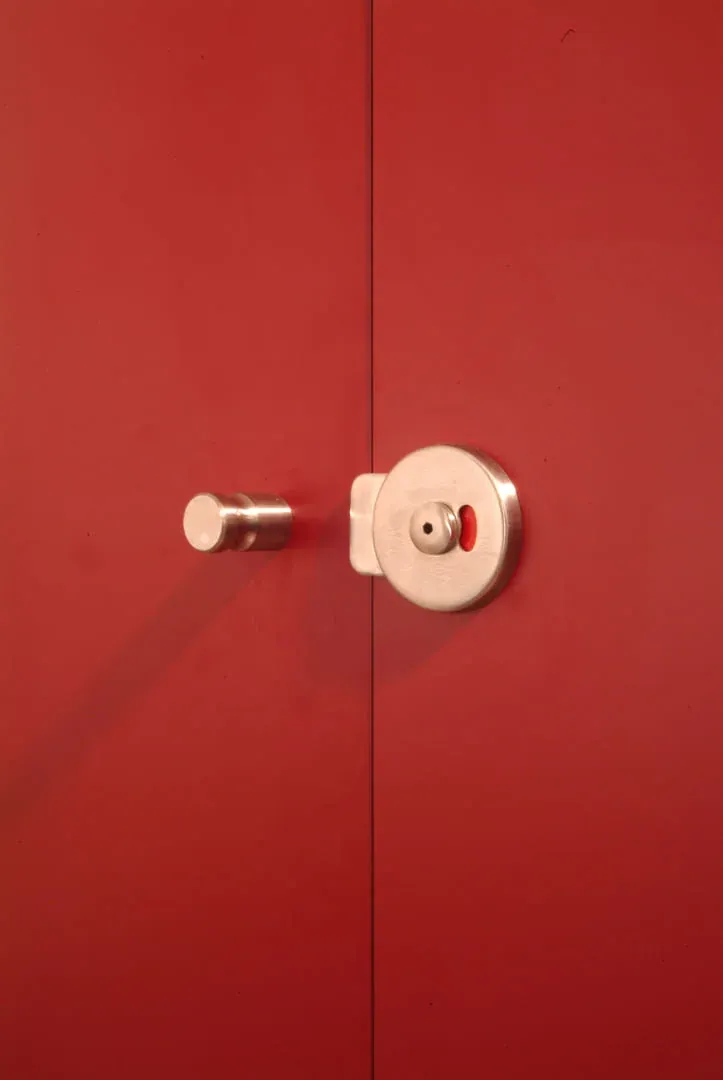 Condena de acero inoxidable con el indicador rojo de ocupado y un pomo, en la puerta roja de una cabina sanitaria