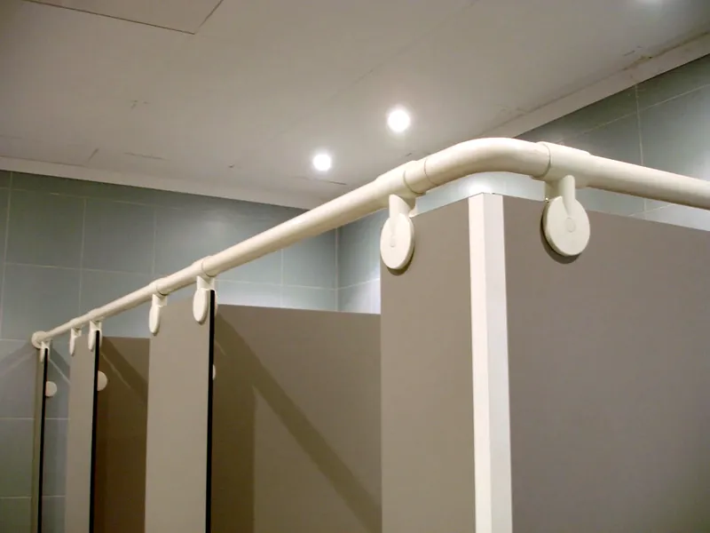Tubo de nylon blanco con su unión en codo y sus pinzas sobre cabinas sanitarias grises
