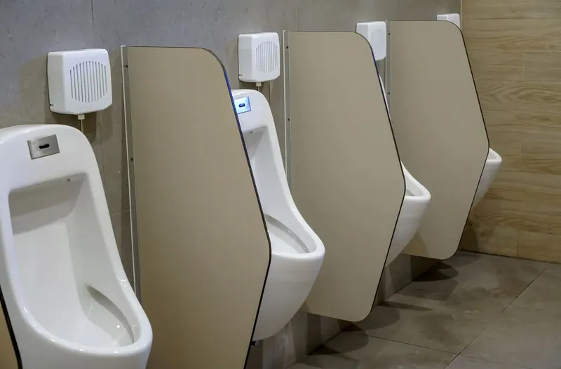 Separadores de urinario de compacto fenólico beige, con el canto recortado en ángulo, entre urinarios de pared