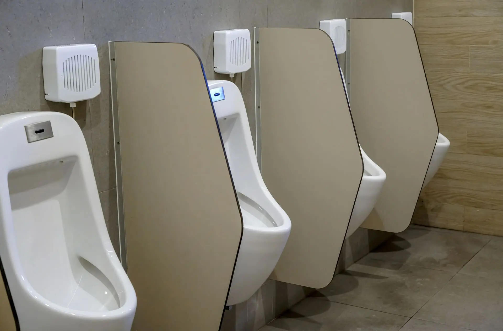 Baño público con separadores fenólicos de color beige instalados entre urinarios blancos, proporcionando privacidad y manteniendo un diseño higiénico y organizado - Bellum Logistics