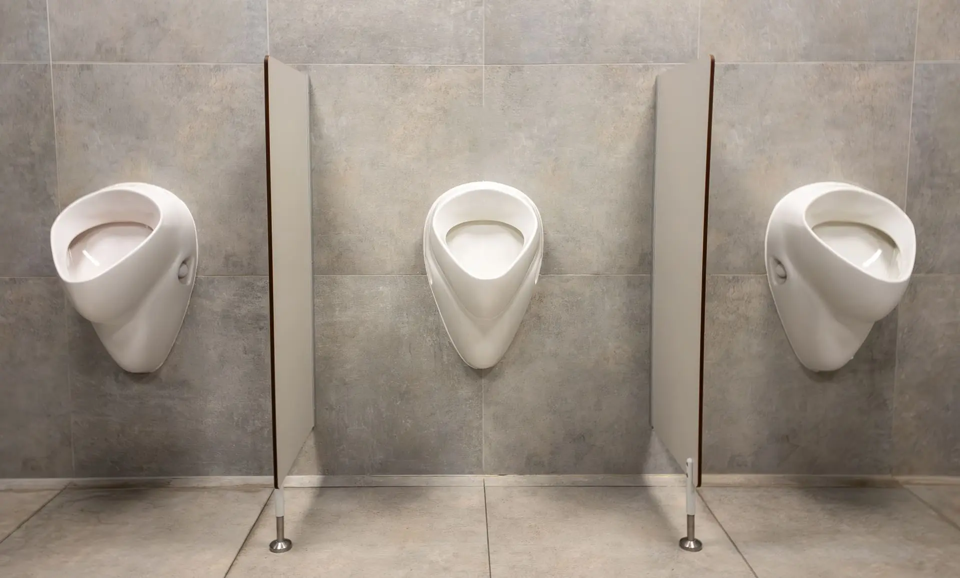 Baño masculino equipado con urinarios blancos y separadores fenólicos de altura completa que llegan hasta el suelo, con soportes metálicos para una máxima privacidad y un estilo minimalista - Bellum Logistics