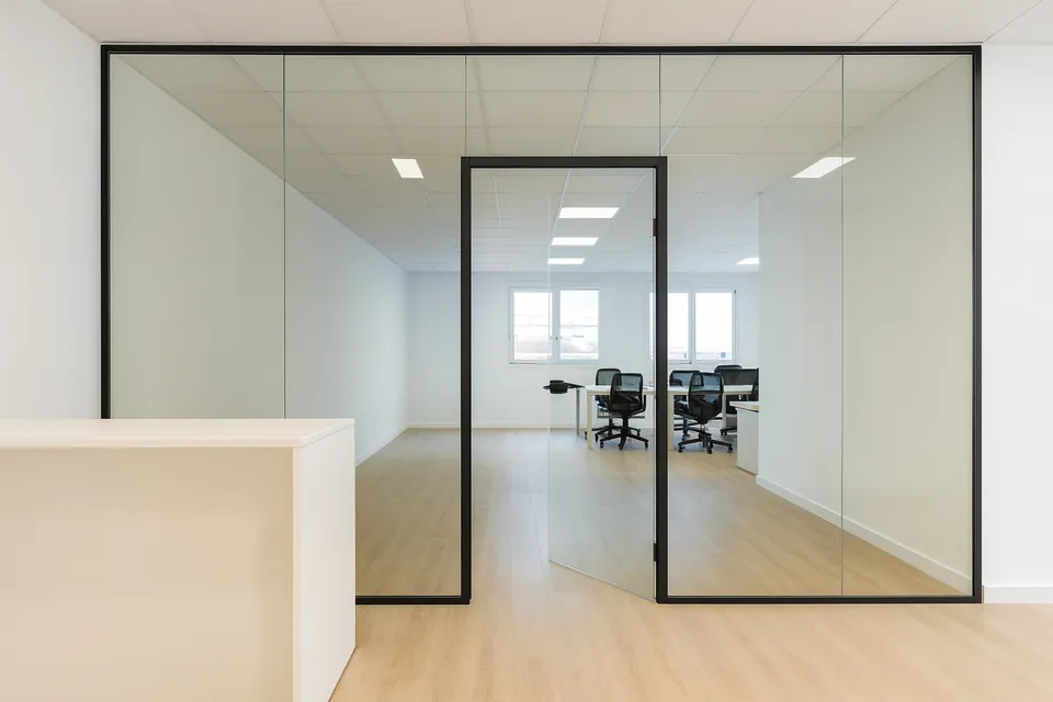 Recepción de oficina separada de la zona de trabajo por una mampara de cristal con puerta de cristal