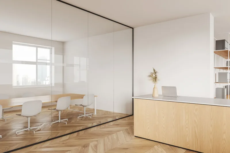 Sala de reuniones cerrada con mampara de cristal de perfil negro, junto a la recepción de una oficina