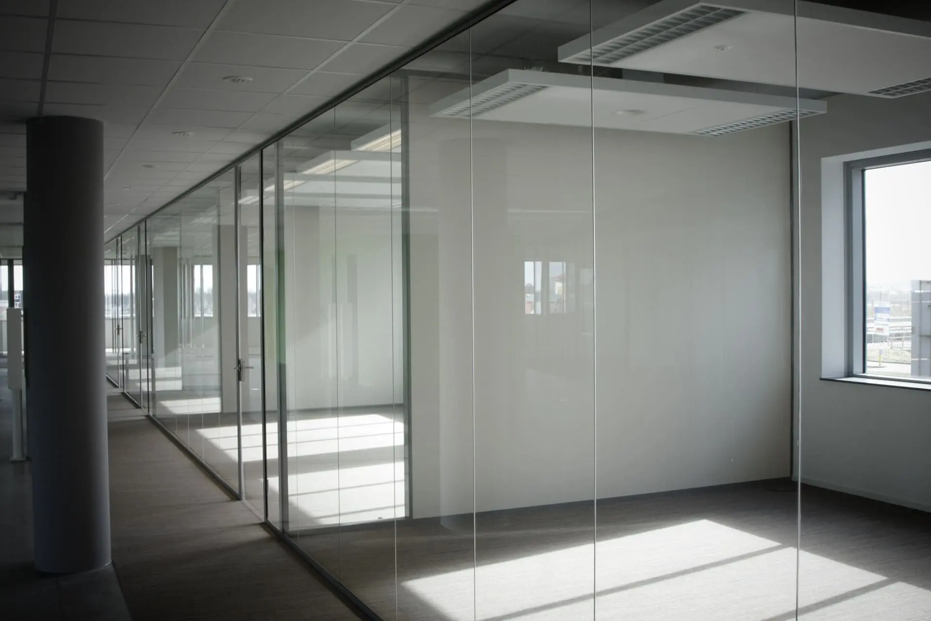 Interior de oficina iluminado con luz natural, separado por elegantes mamparas de cristal transparente que proporcionan un entorno de trabajo limpio y abierto - Bellum Logistics