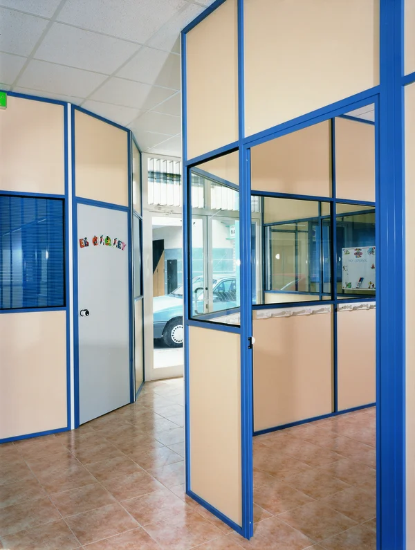 Entrada a zona de oficinas con puertas de cristal azul y mamparas monopanel que ofrecen un aspecto profesional y acogedor - Bellum Logistics