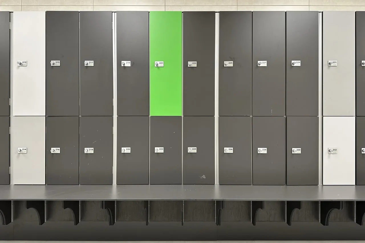 Taquillas de dos puertas en gris antracita, blanco y verde, cada una con su placa numerada y su cerradura RFID Ojmar OTS 10 Básica, con el banco incorporado: un asiento antracita sobre cartelas